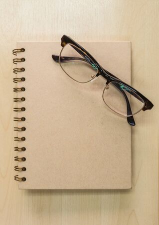 Brown notebook with eyeglasses on wood background under window lightの写真素材