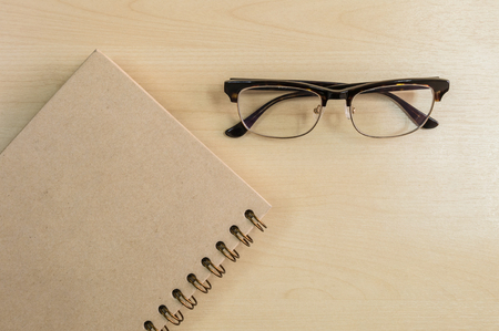 Brown notebook with eyeglasses on wood background under window lightの写真素材