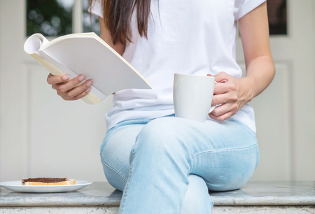 Asian woman sitting on marble chair in front of house for have breakfast and read a book in the morningの写真素材