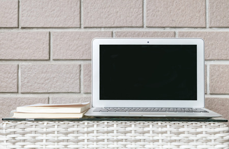 Closeup computer on blurred wood weave table and brown brick wall texture background , beautiful work place interior of house conceptの写真素材