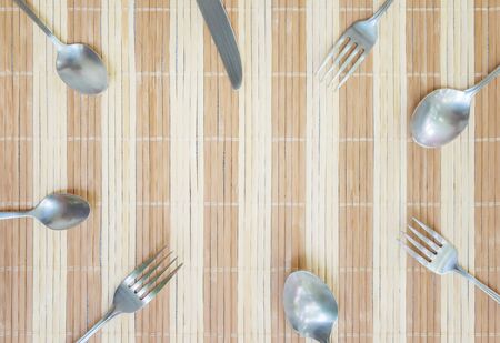 Closeup group of  stainless fork spoon and knife on wood mat textured background with copy space at the center in top viewの写真素材