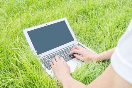 Asian woman lied on grass floor in the garden textured background for use a notebook computer , work...