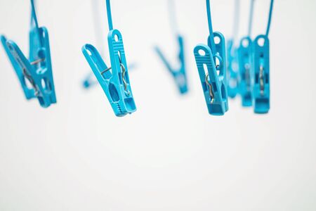 Closeup colorful hanged blue clothespin for dry clothes in the sun on blurred white cement textured background in selective focusの写真素材
