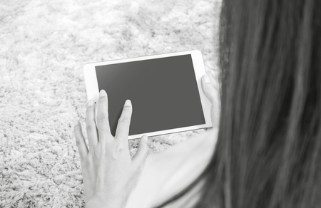 Closeup tablet computer on asian woman hand on blurred gray carpet floor textured background with copy space in black and white toneの写真素材