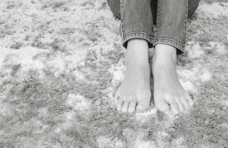 Closeup foot of asian woman sitting on gray carpet floor textured background in house in black and white toneの写真素材