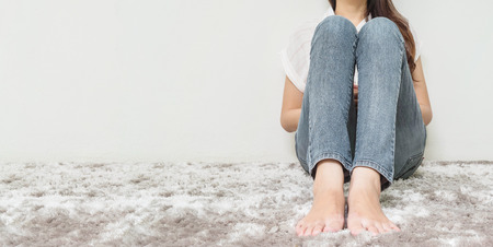 Asian woman sit on gray carpet floor with white cement textured background at the corner of house with copy spaceの写真素材