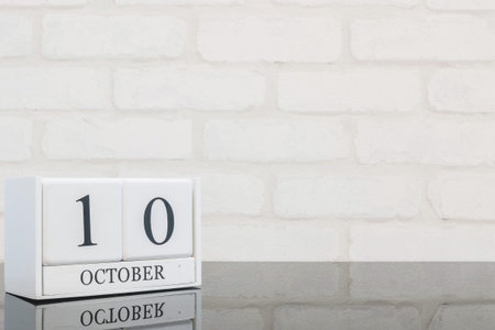 Closeup white wooden calendar with black 10 october word on black glass table and white brick wall...