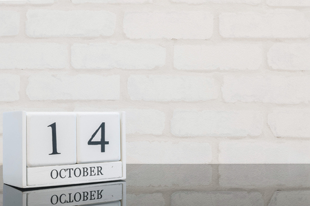 Closeup white wooden calendar with black 14 october word on black glass table and white brick wall textured background with copy space , view another more date in my portfolioの写真素材