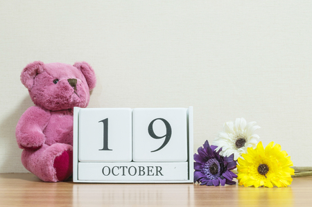 Closeup surface white wooden calendar with black 19 october word on brown wood desk and cream color wallpaper in room textured background with copy space , view another more date in my portfolioの写真素材