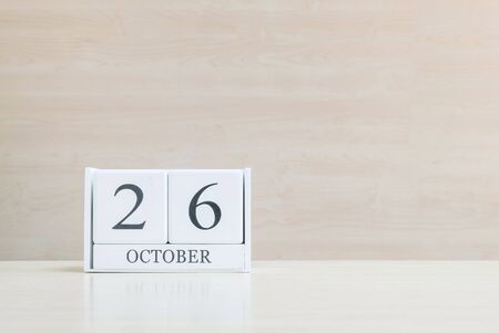 Closeup surface white wooden calendar with black 26 october word on blurred brown wood desk and wood wall textured background with copy space , selective focus at the calendarの写真素材