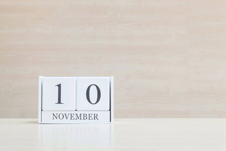 Closeup surface white wooden calendar with black 10 november word on blurred brown wood desk and wood wall textured background with copy space , selective focus at the calendarの写真素材