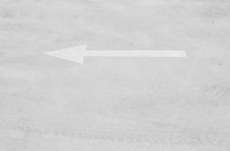 Closeup white painted arrow sign on cement street floor textured background in black and white tone...