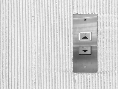Closeup surface elevator button in up and down arrow sign on cement wall textured background in black and white tone with copy spaceの写真素材