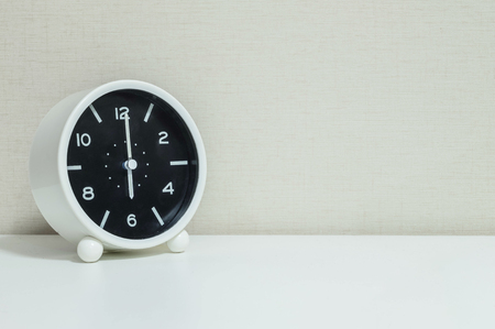 Closeup black and white alarm clock for decorate in 6 o'clock on white wood desk and cream wallpaper textured background with copy spaceの写真素材