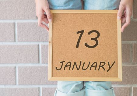 Closeup calendar at the cork board in hand of asian woman in front of her legs with 13 january word on brick wall textured backgroundの写真素材
