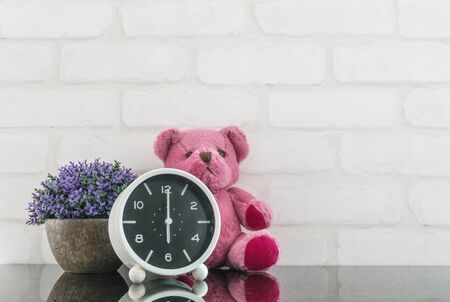 Closeup black and white alarm clock for decorate in 6 o'clock with bear doll and plant on black glass table and white brick wall textured background with copy spaceの写真素材