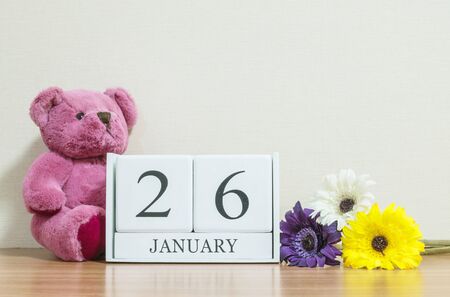 Closeup surface white wooden calendar with black 26 january word on brown wood desk and cream color wallpaper in room textured background with copy space , selective focus at the calendarの写真素材