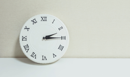 Closeup white clock for decorate show a quarter past two p.m. or 2:15 p.m. on white wood desk and cream wallpaper textured background with copy spaceの写真素材