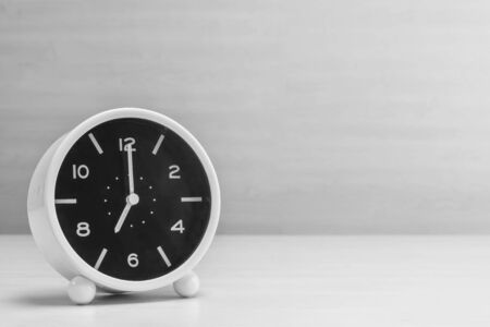 Closeup alarm clock for decorate in 7 o'clock on wood desk and wall textured background in black and white tone with copy spaceの写真素材