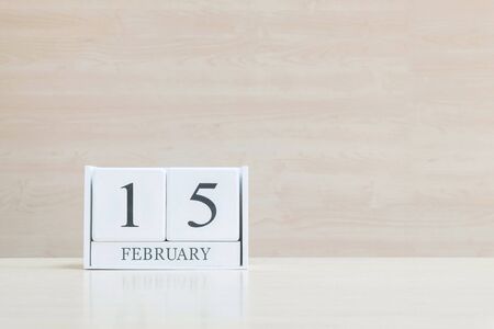 Closeup surface white wooden calendar with black 15 february word on blurred brown wood desk and wood wall textured background with copy space in selective focus at the calendarの写真素材