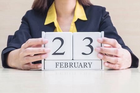 Closeup white wooden calendar with black 23 february word in blurred working woman hand on wood desk in office room in selective focus at the calendarの写真素材