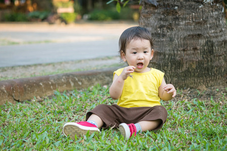 Closeup cute asian kid pick up hay into his mouth on grass floor in the park backgroundの写真素材