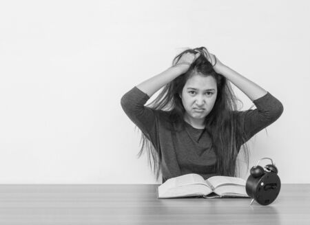 Closeup asian woman sitting for read a book with strain face emotion on wood table and white cement wall textured background in black and white tone with copy spaceの写真素材