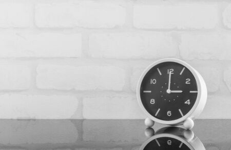 Closeup black and white alarm clock for decorate in 3 o'clock on black glass table and white brick wall textured background in black and white tone with copy spaceの写真素材