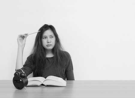 Closeup asian woman tired from reading a book with thinking face emotion in work concept on wood table and white cement wall textured background in black and white tone with copy spaceの写真素材