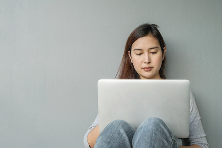 Closeup asian woman sitting for use computer notebook in work concept on blurred cement wall textured background with copy spaceの写真素材