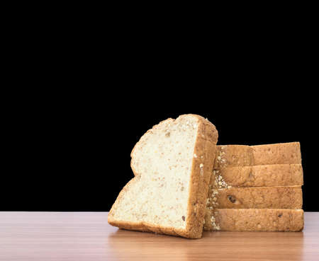 Closeup pile of wheat bread for breakfast on brown wood desk isolated on black backgroundの写真素材