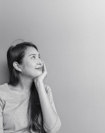 Closeup asian woman sitting and look at space with smile face on blurred cement wall textured background in black and white tone with copy spaceの写真素材