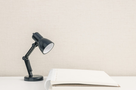 Closeup black small lamp on blurred white wood desk and cream wallpaper wall textured background with copy spaceの写真素材