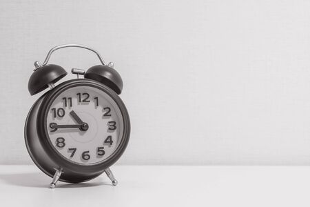 Closeup alarm clock for decorate show a quarter to eleven o'clock or 10:45 a.m. on white wood desk and cream wallpaper textured background in black and white tone with copy spaceの写真素材