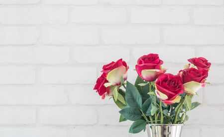 Closeup artificial fabric red rose flower for decorate on white brick wall textured background with copy spaceの写真素材