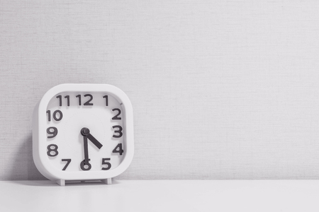 Closeup white clock for decorate show half past four o'clock or 4:30 p.m. on white wood desk and cream wallpaper textured background in black and white tone with copy spaceの写真素材