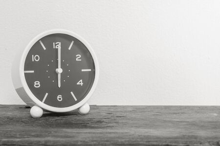 Closeup alarm clock for decorate in 6 o'clock on old wood desk and white cement wall textured background in black and white tone with copy spaceの写真素材