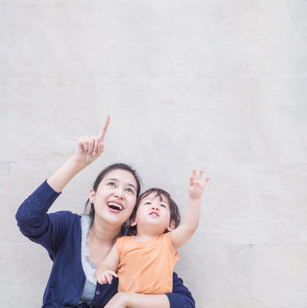 Closeup asian mother and son point to copy space of picture on marble stone wall textured background