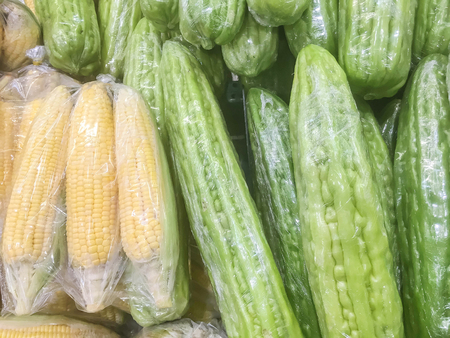 Closeup surface pile of fresh green bitter cucumber and corn in plastic rap for sell textured backgroundの写真素材