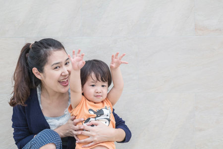 Closeup asian mother and son in happy motion on marble stone wall textured background with copy spaceの写真素材