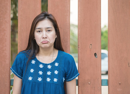 Asian woman with sad face emotion on blurred wooden fence backgroundの写真素材