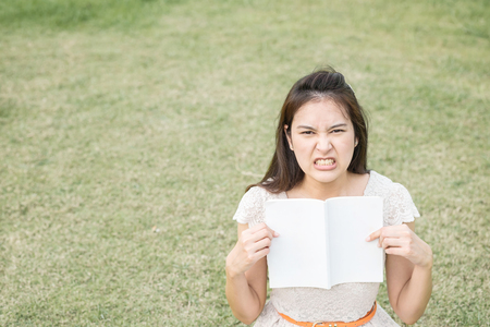 Asian woman with stress emotion with a book in hand on blurred grass floor backgroundの写真素材