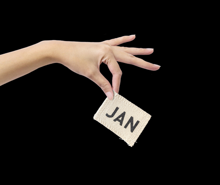 Closeup action of woman hand catching and hold small picec of fabric calendar in JAN month in hand isolated on black backgroundの写真素材