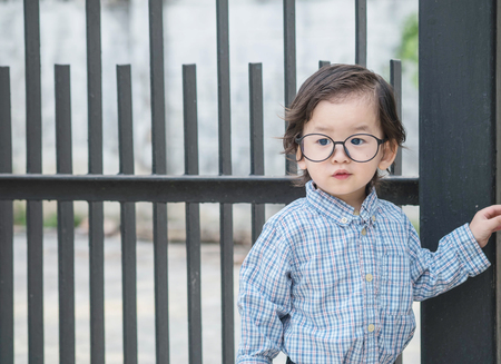 Closeup asian kid with eyeglasses stand in front of steel fence textured backgroundの写真素材