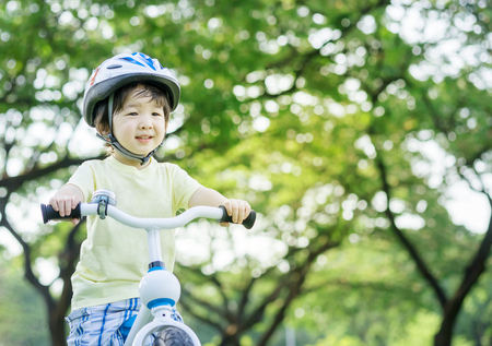Closeup cute Asian kid ride a bicycle on green tree in the park textured background with copy spaceの写真素材