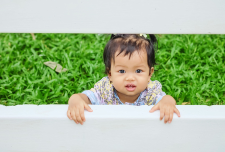 Closeup little girl catch a white fence on grass floor in the garden background with smile faceの写真素材