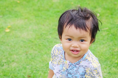 Closeup little girl with smile face stand on grass floor in the park background with copy spaceの写真素材