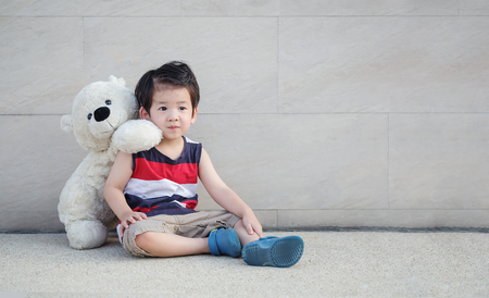 Closeup asian kid with bear doll sit at pathway on marble stone wall textured background with copy spaceの写真素材