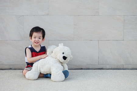 Closeup asian kid with bear doll sit at pathway on marble stone wall textured background with copy spaceの写真素材