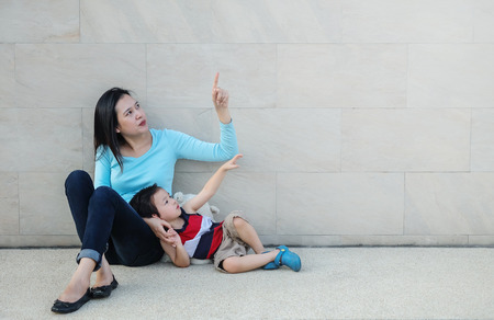 Closeup asian mother pointing her finger and tell her son to look at space on marble stone wall textured backgroundの写真素材